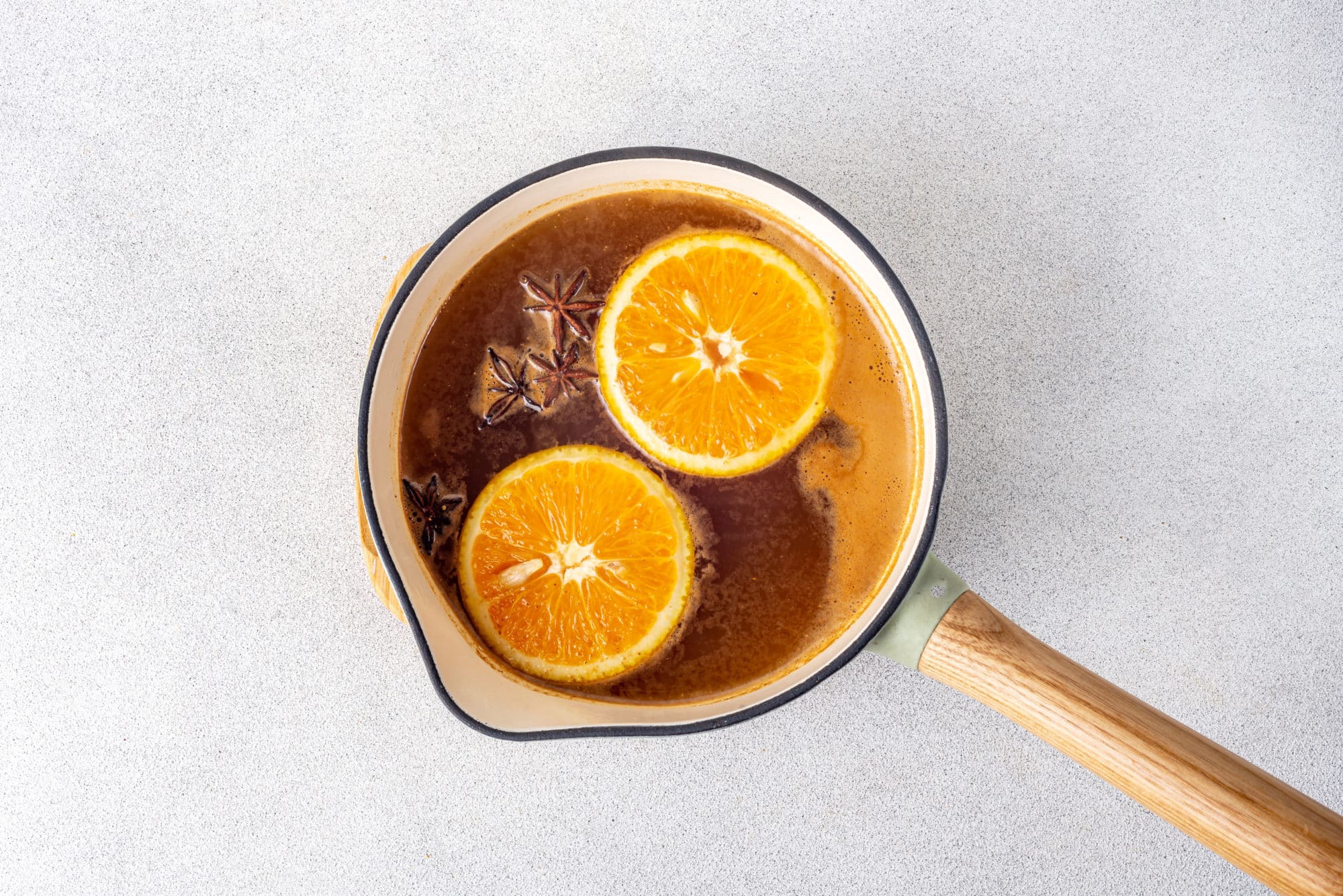 a pot cooking apple cider with floating orange slices and star anise.