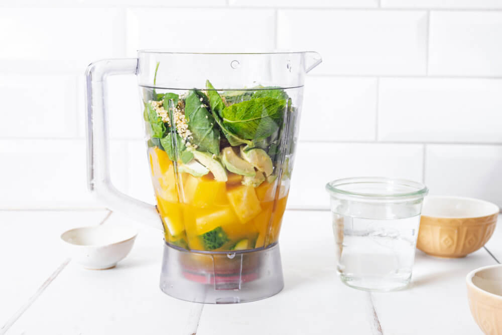 citrus smoothie ingredients in a blender with a glass of water on the side.