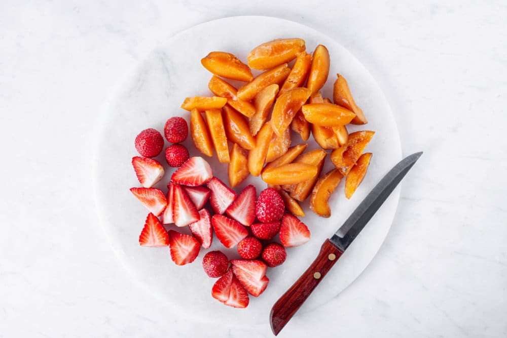 Sliced fresh fruit on a white cutting board with a knife.