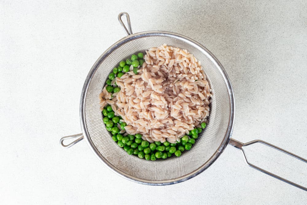 Washed orzo and peas in a sieve.