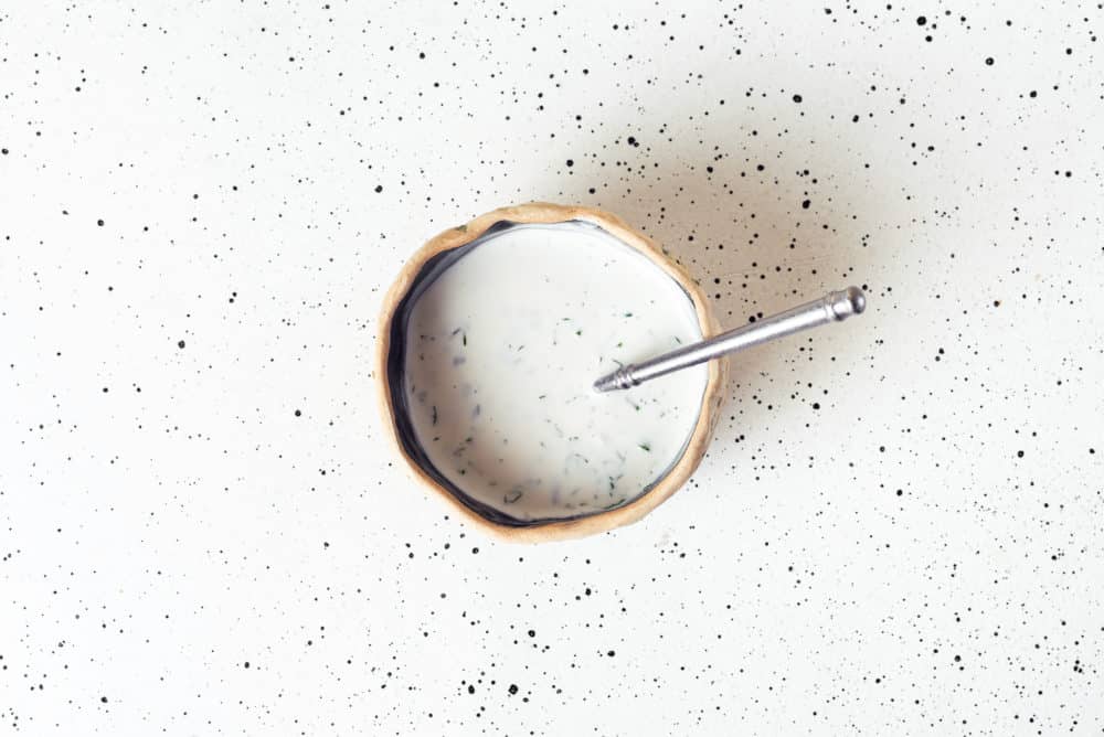 A bowl of dressing with a spoon.