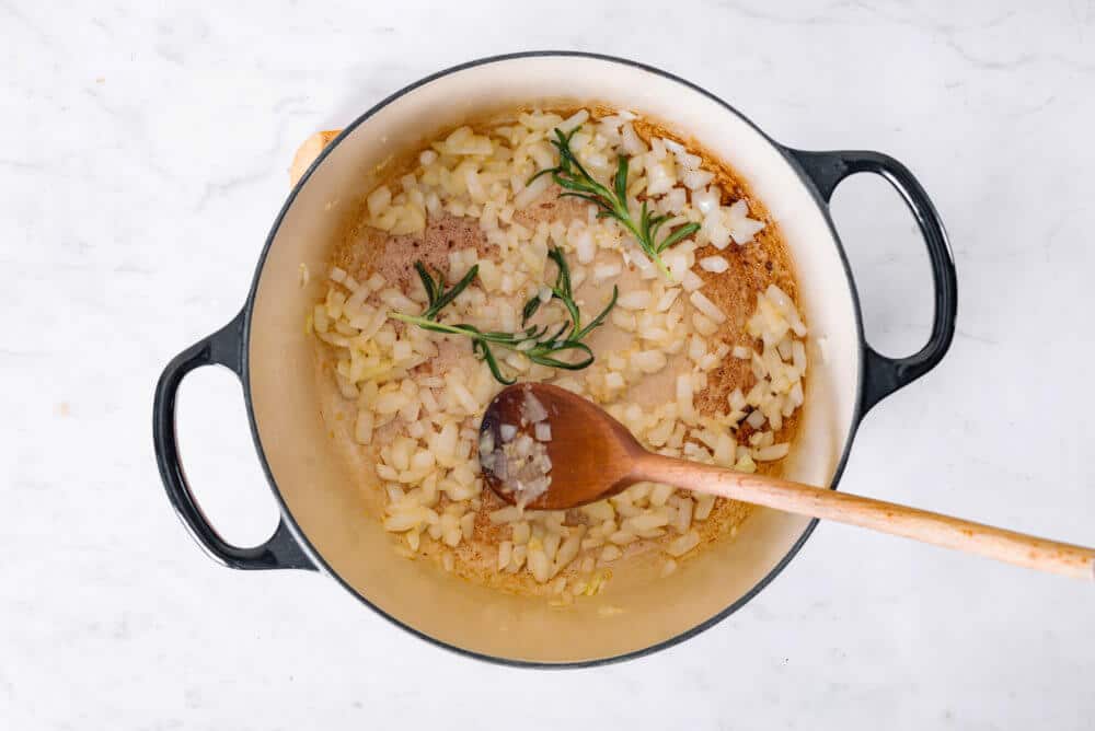 onion and rosemary in a soup pot with a wooden spoon.