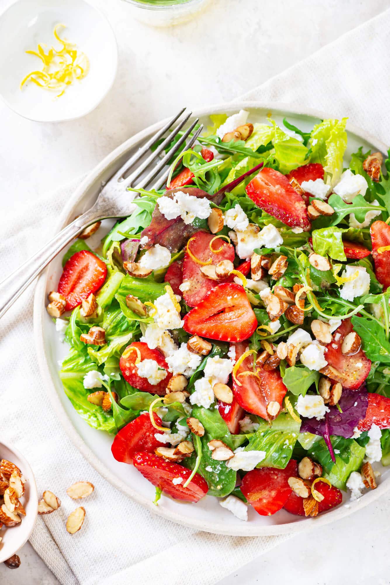 Summer berry salad on a white plate with a fork and lemon zest on the side.