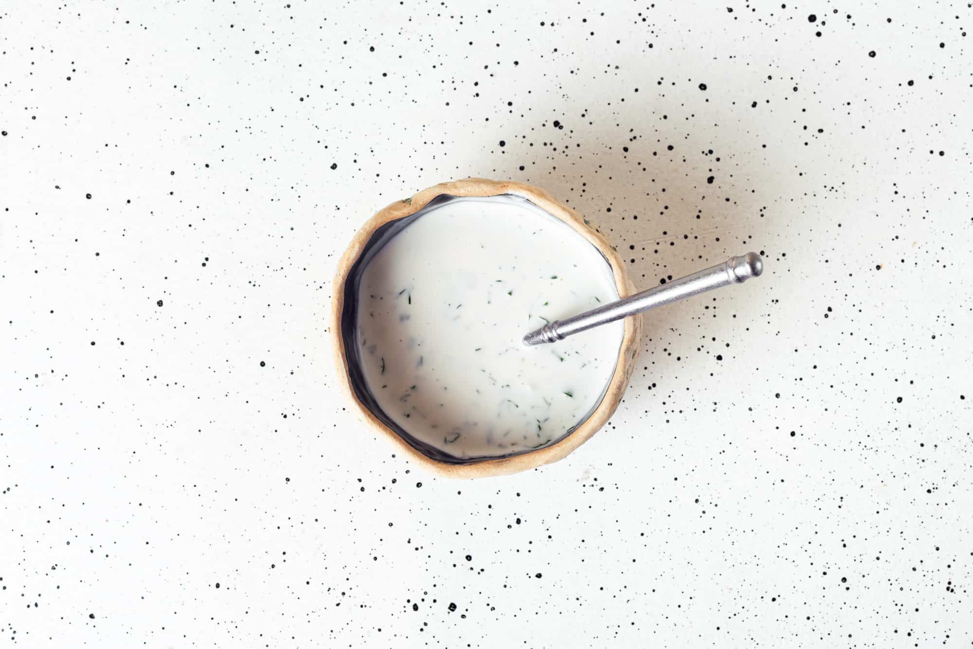 A bowl of dressing with a spoon.