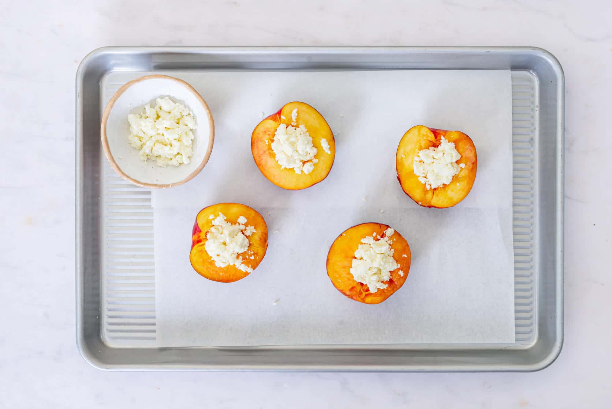 unbaked-nectarines-on-parchment-paper-on-a-baking-tray-with-a-bowl-of-goat-cheese-on-the-side