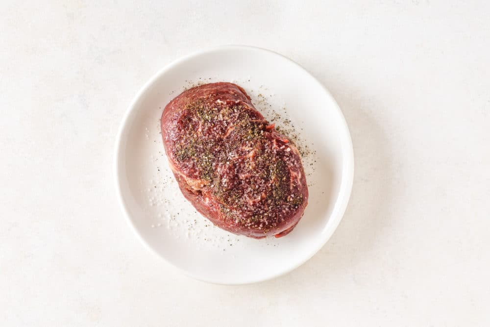 a white plate with steak on it covered in spices black pepper and salt.