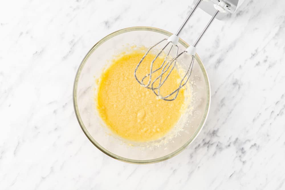 a glass bowl with an egg sugar mixture and hand mixers.