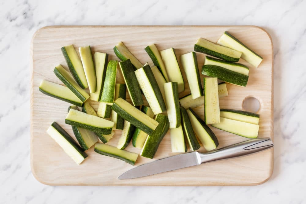 Zucchini sliced on a wooden board with a knife on the side.