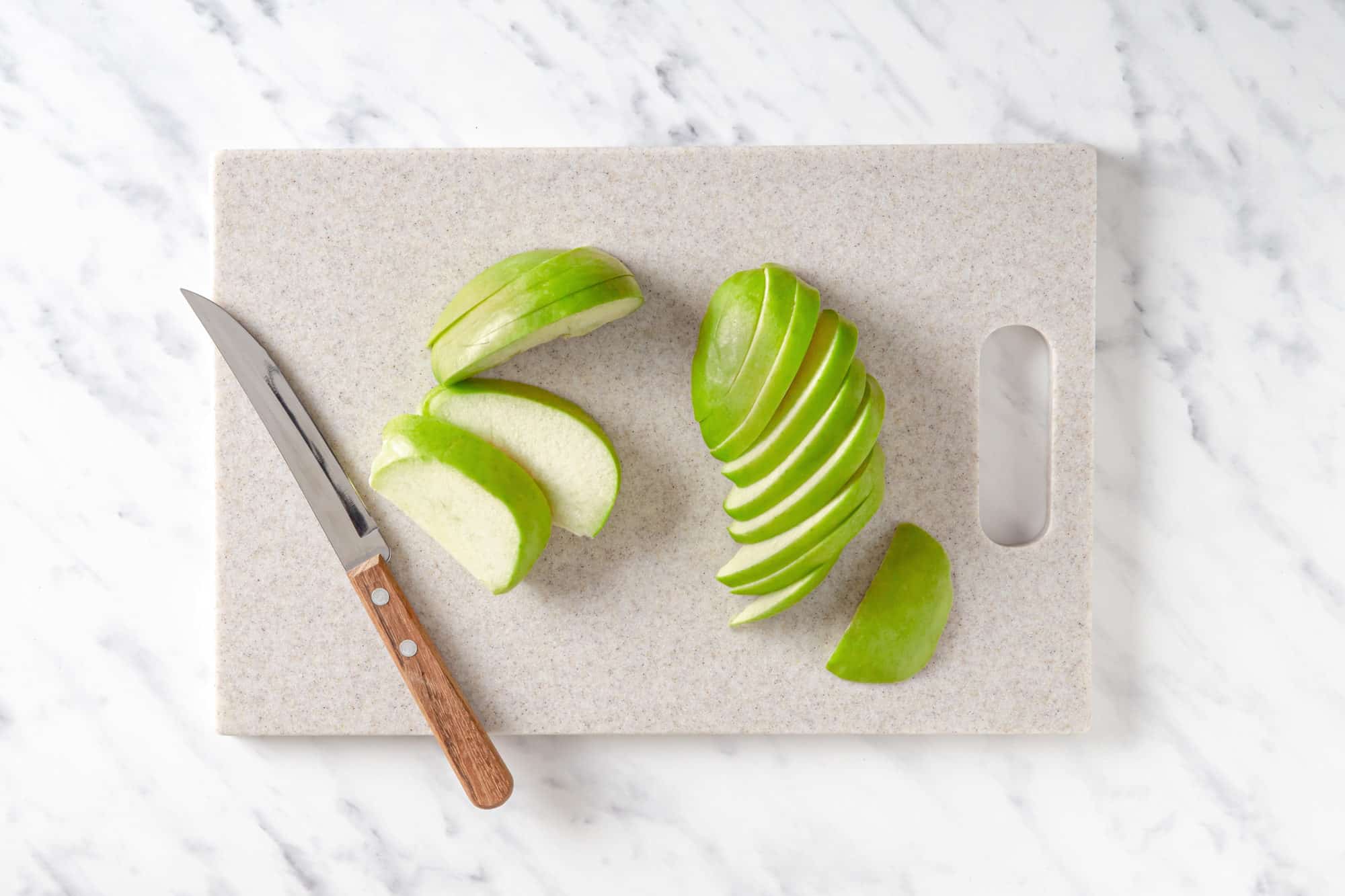 a cutting board with a knife and thinly sliced apple.