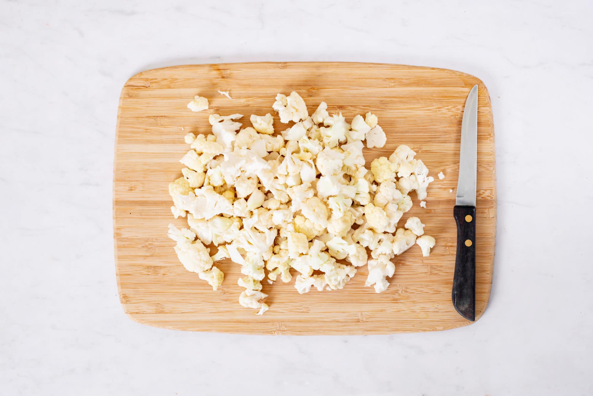 Chopped cauliflower on a wooden board with a knife.