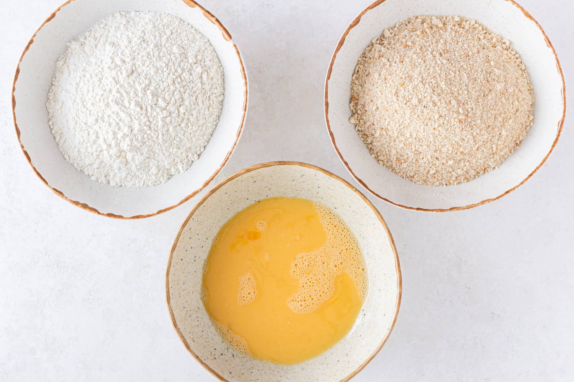 three bowls with separate ingredients flour egg and bread crumbs in the bowls.