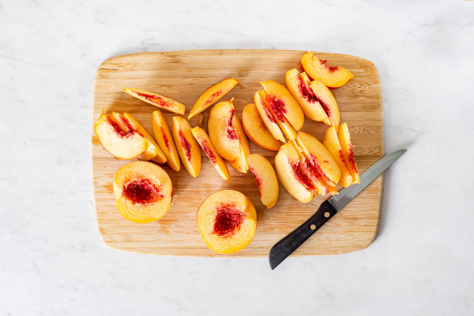 Peaches sliced and chopped on a board with a knife.