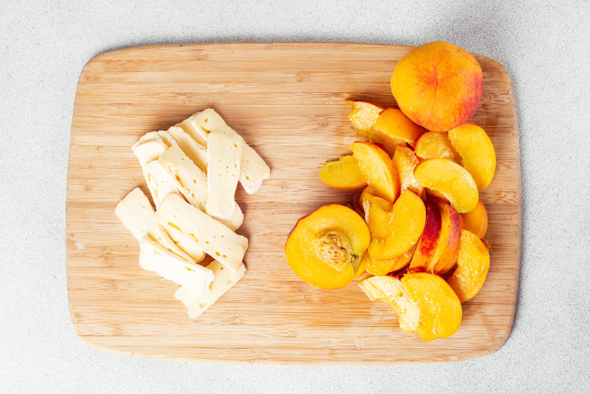 A wooden cutting board with peaches and brie on it.