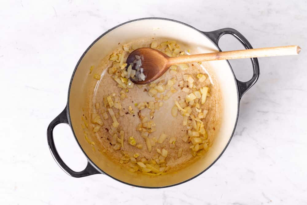 a large pot with onion sauteing inside it with a wooden spoon.