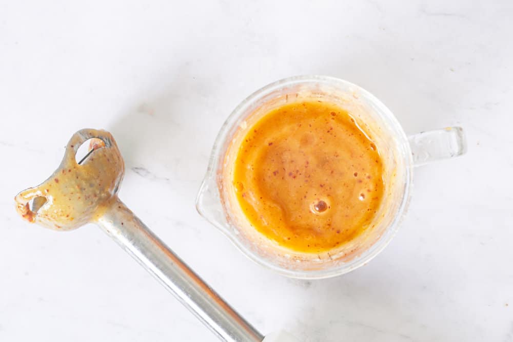 pureed peaches in a glass cup with an immersion blender on the side.