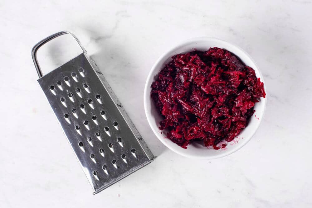 Shredded beets in a white plate with a grater on the side.