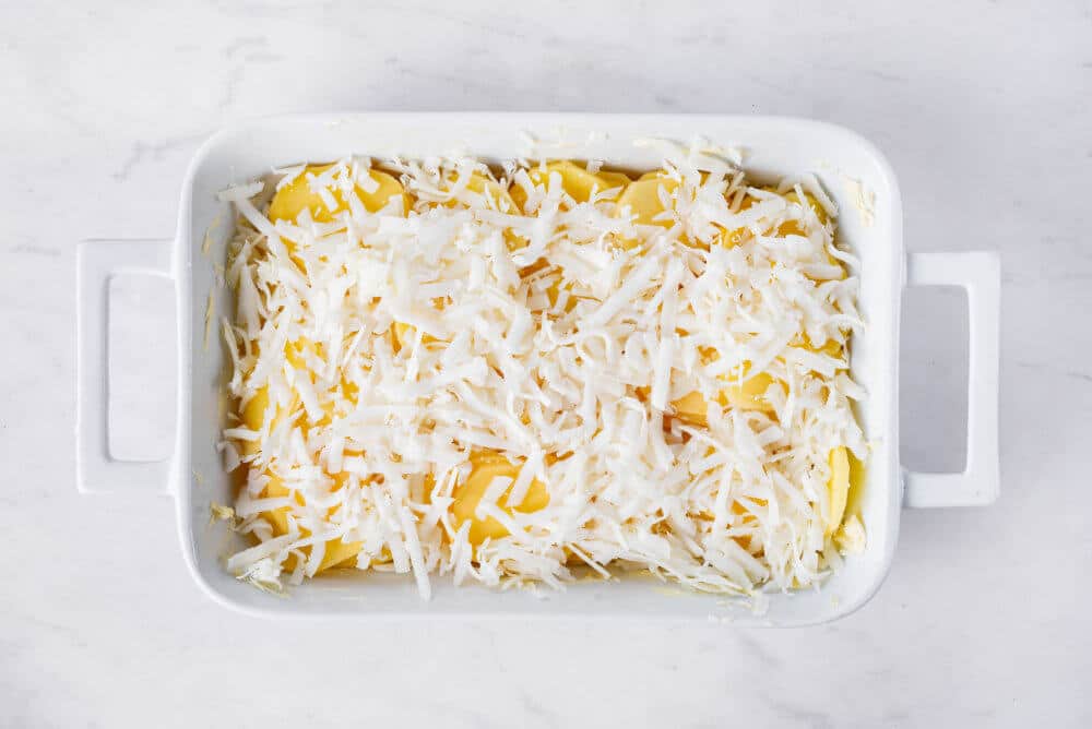 scalloped potatoes with cheese on top in a white rectangular baking tray ready to bake.