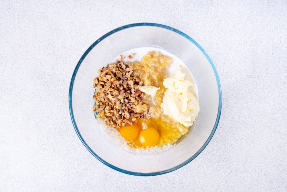 a glass bowl with ingredients for banana bread in it.