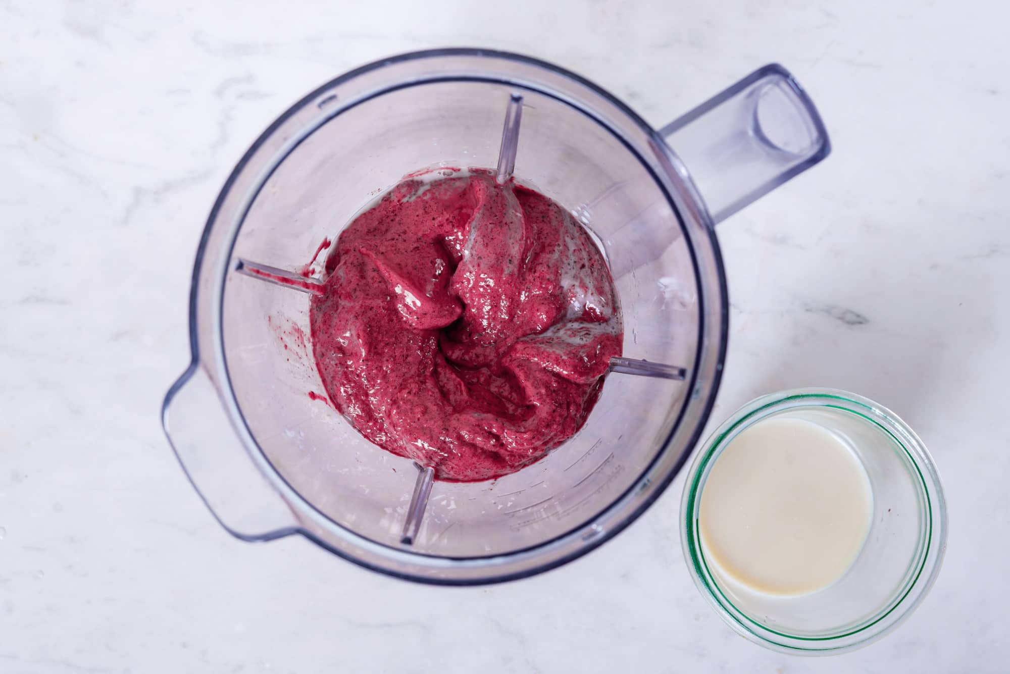 Acai smoothie in a blender with a clear glass of milk on the side.