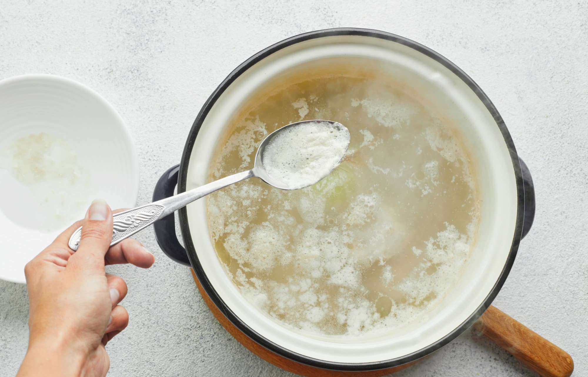 chicken-cooking-in-a-soup-pot-on-a-wooden-board-with-a-spoon-removing-the-foam-on-top