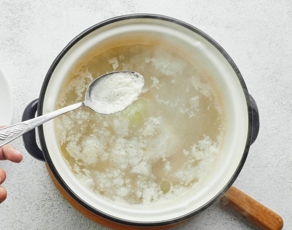 chicken-cooking-in-a-soup-pot-on-a-wooden-board-with-a-spoon-removing-the-foam-on-top