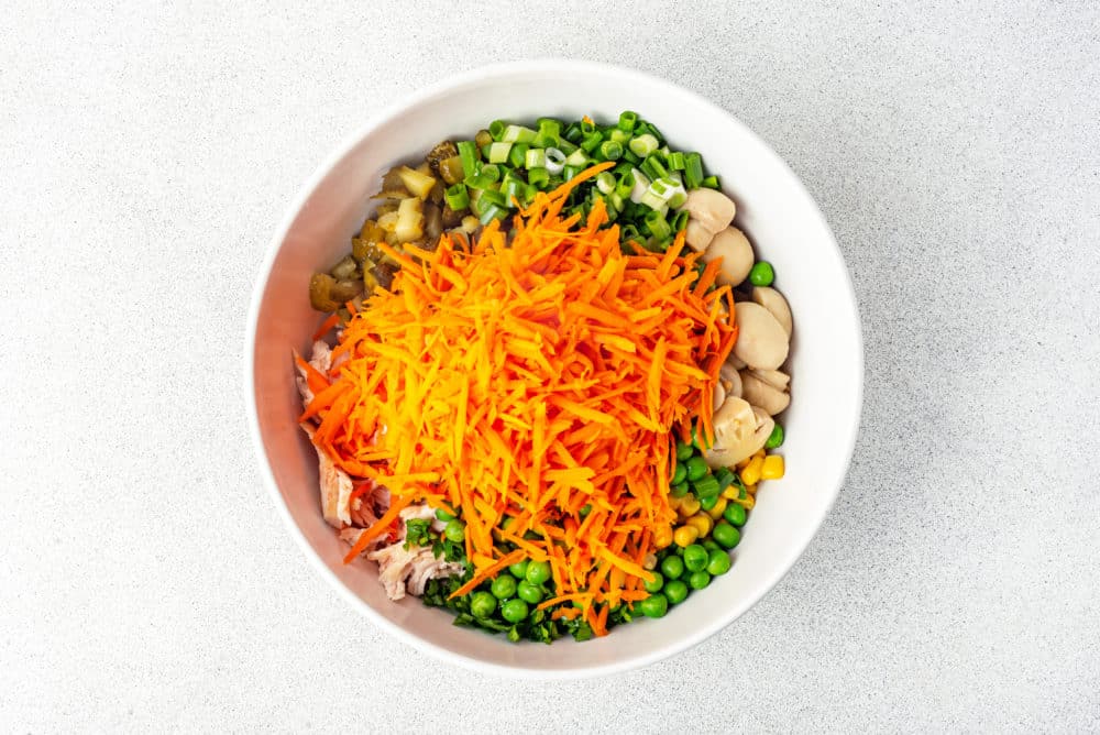 salad ingredients in a white bowl with grated carrots added on top.