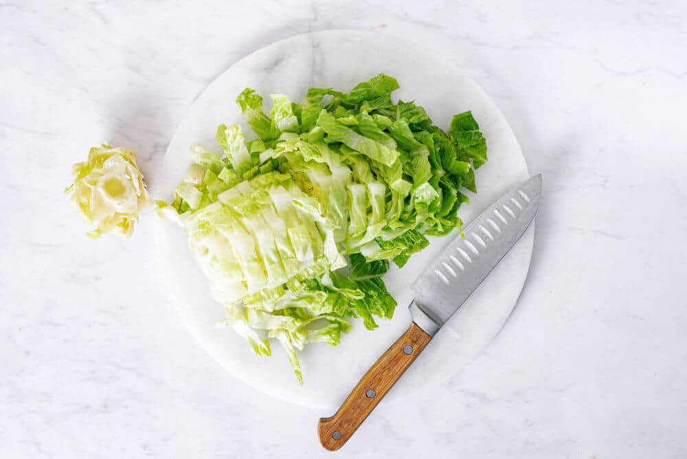 Chopped romaine lettuce on a board with a knife.