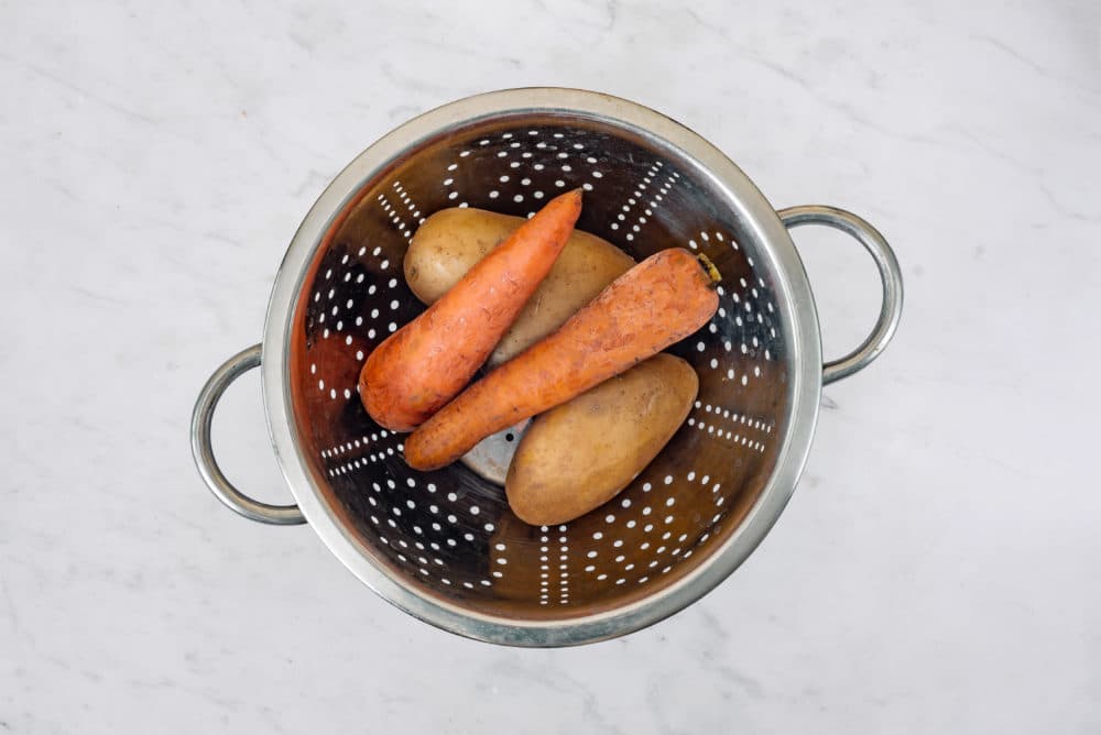 Potatoes and carrots in a silver sieve.