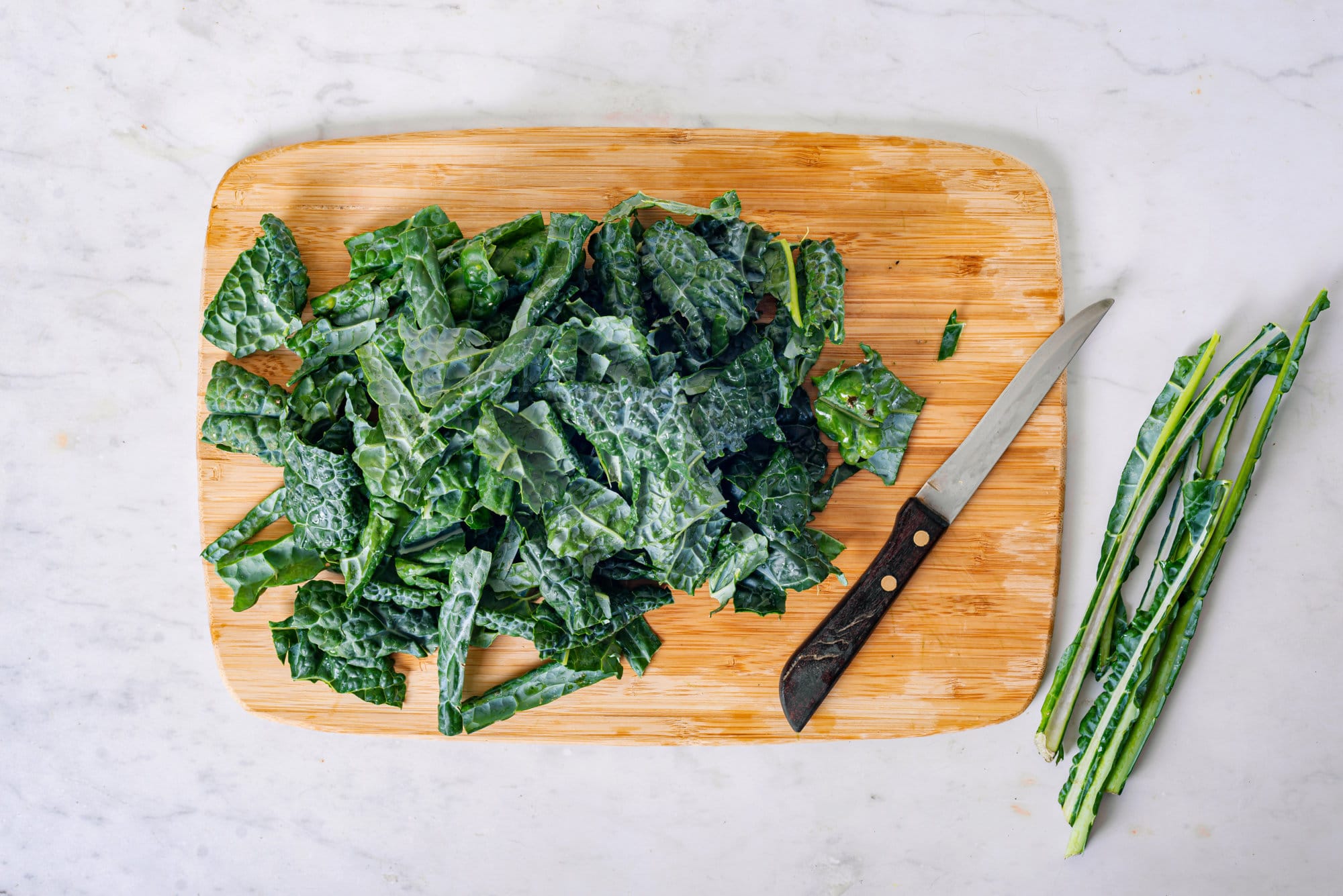 Chopped kale on a wooden board with the stalks and a knife on the side.