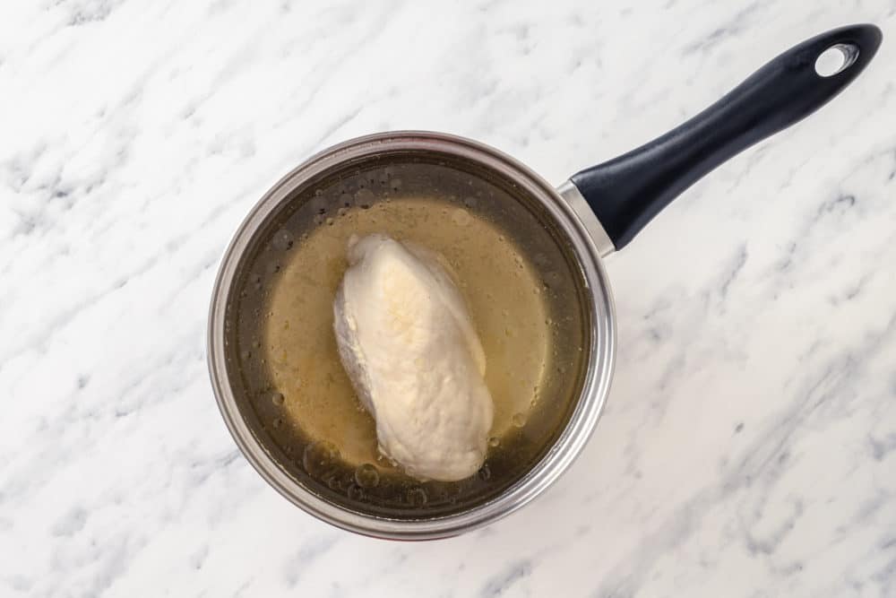 chicken breast boiling in a pot with broth or water.