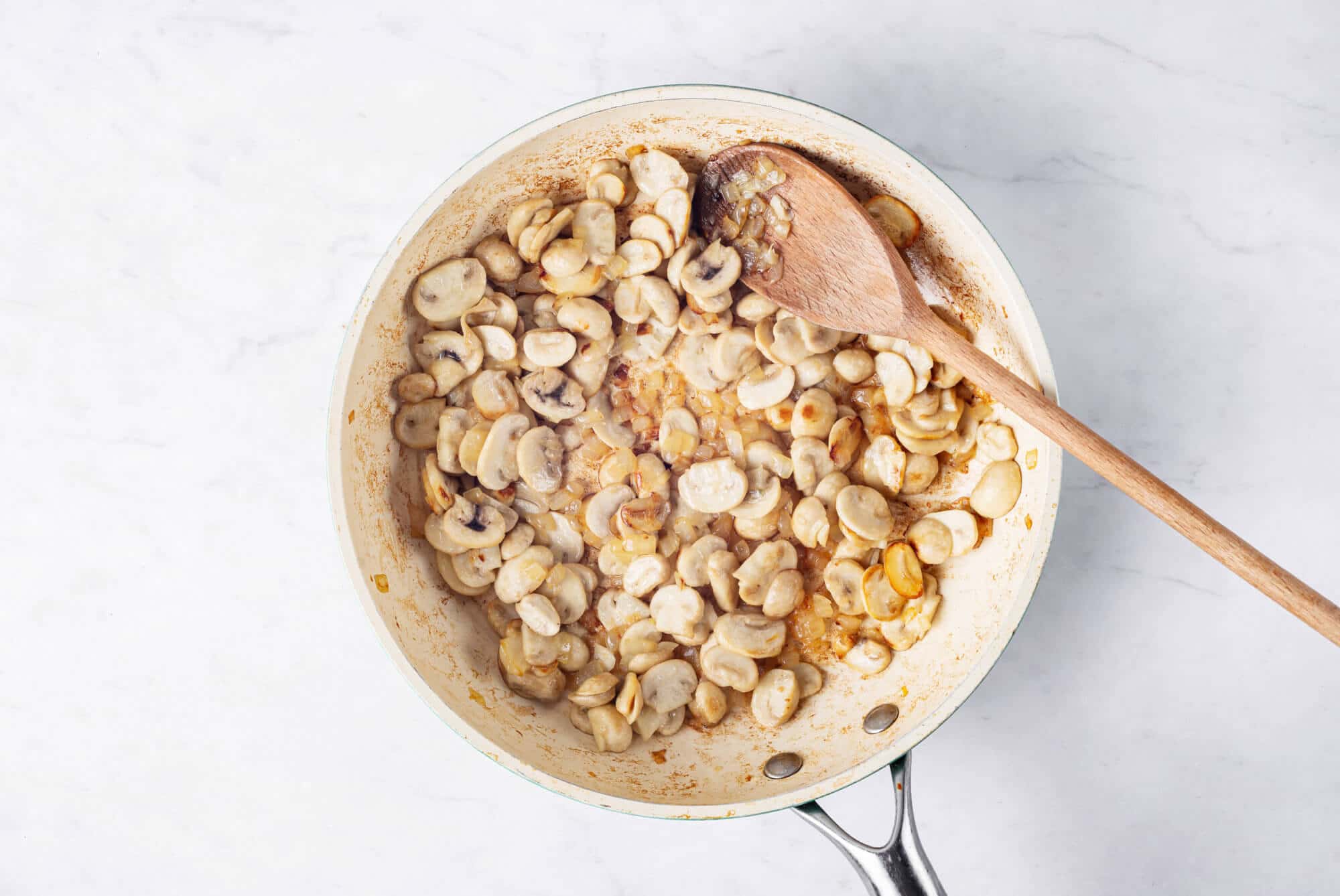 Mushrooms browning in a skillet, mixing with a wooden spoon.