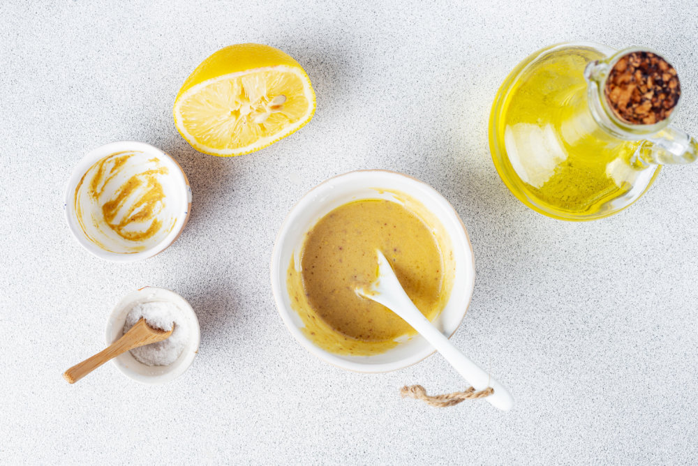 Dijon dressing ingredients from bowls mixed together in a center bowl with a spoon.