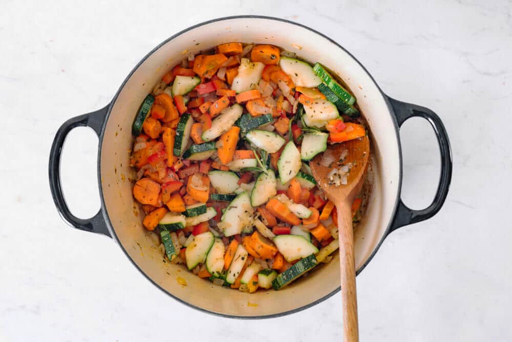 vegetables cooking in a pot with a wooden spoon.