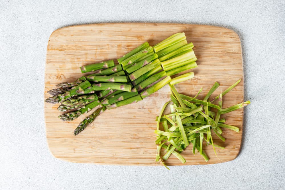 A wooden cutting board with chopped asparagus on it.