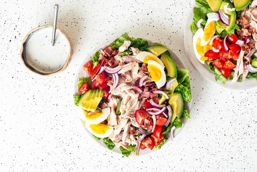 Chicken cobb salad on a white plate with ranch on the side.