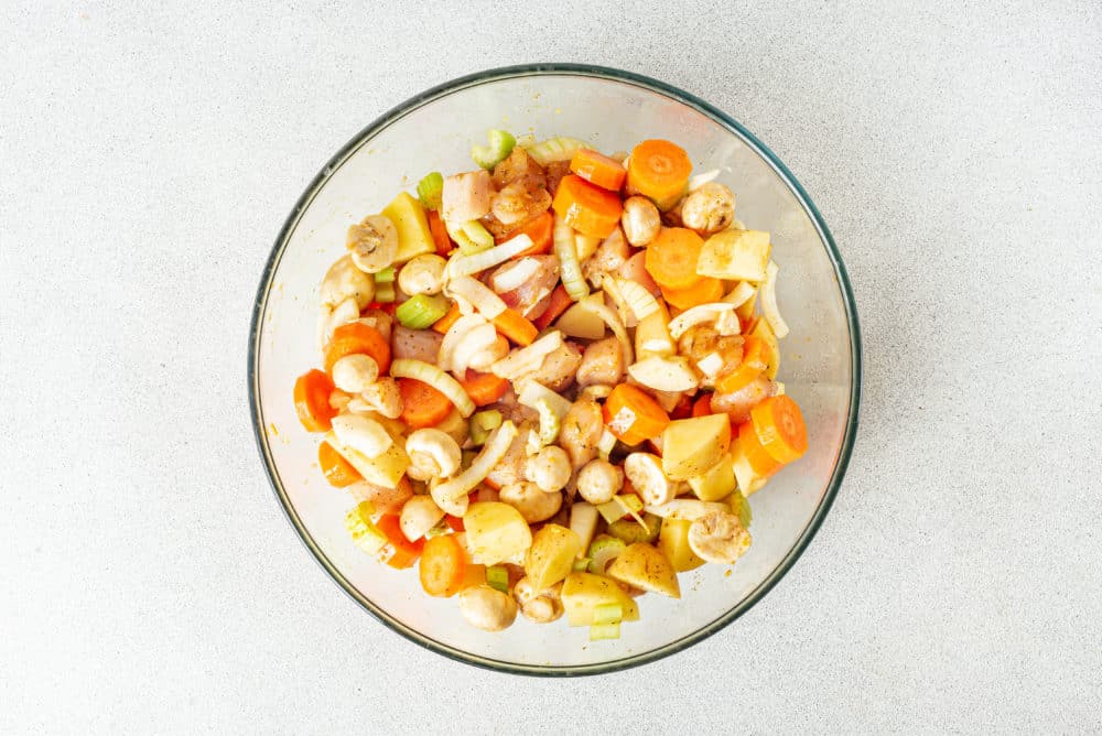 a glass bowl filled with mixed spices in chicken and chopped vegetables.