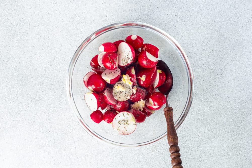 radishes in a glass bowl with a spoon and seasoning mix.