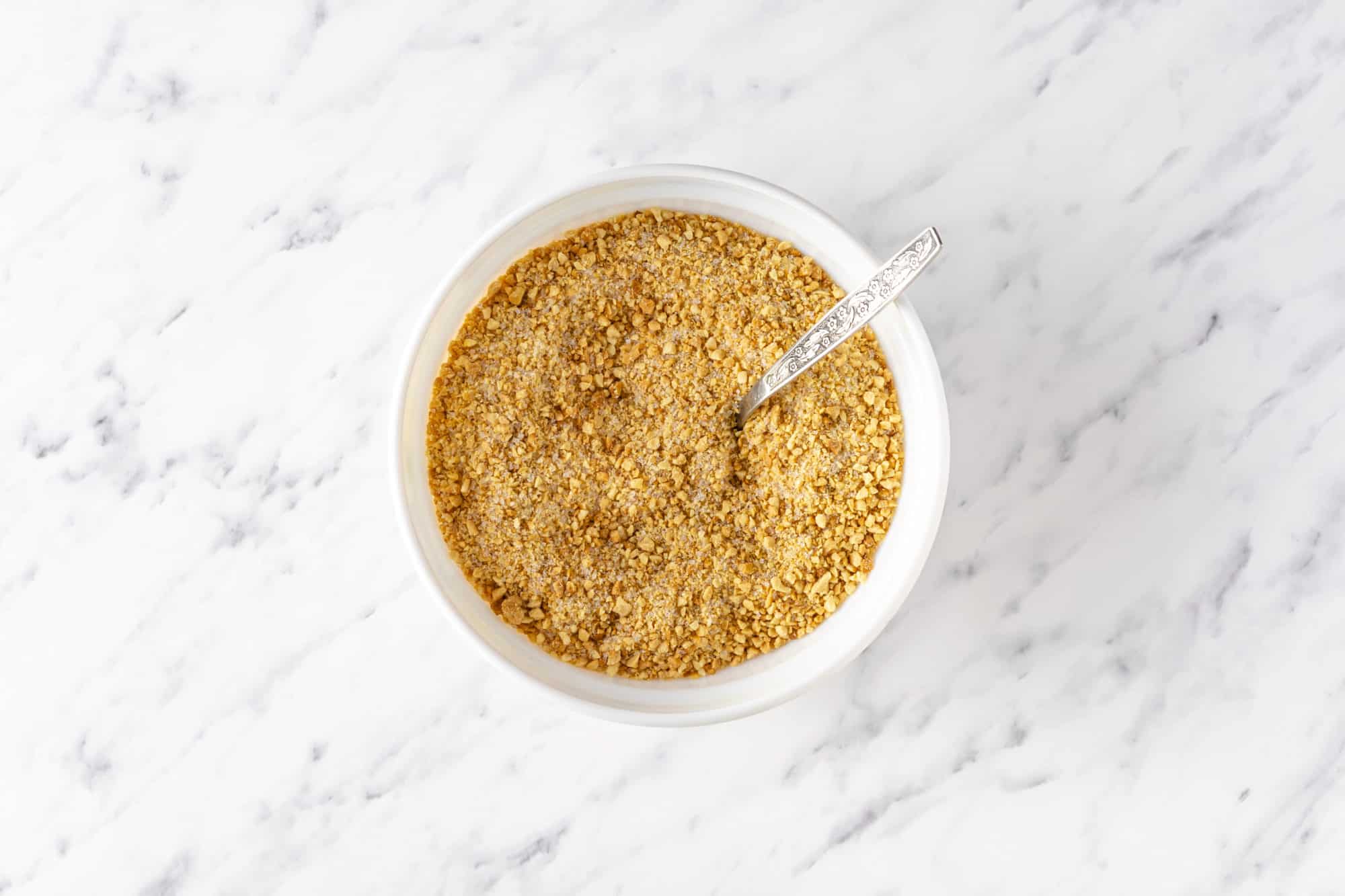 a white bowl with walnut and sugar mixture in it with a spoon.