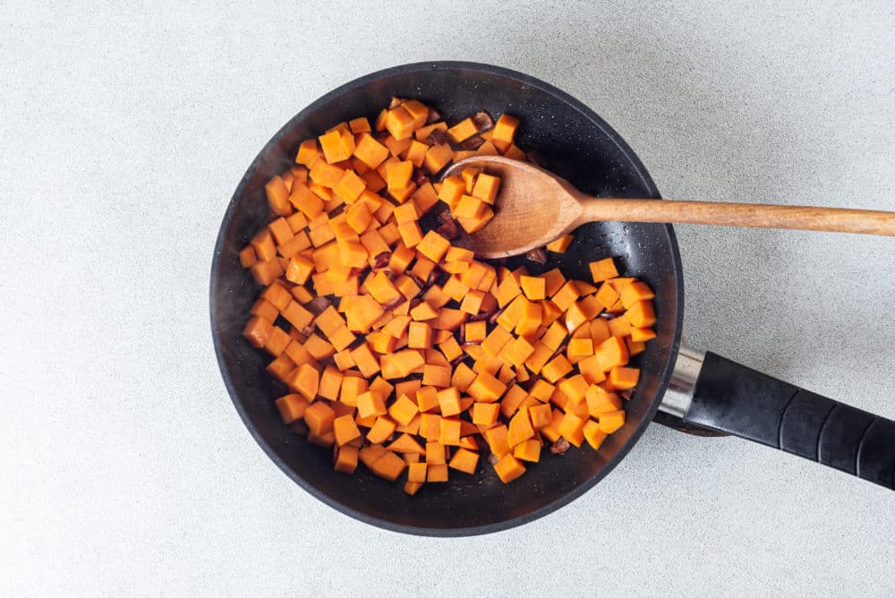 Sweet potatoes cooking in a skillet with a wooden spoon.