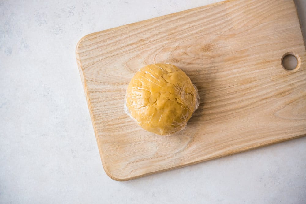 a wooden board with a ball of dough on it wrapped in plastic wrap.