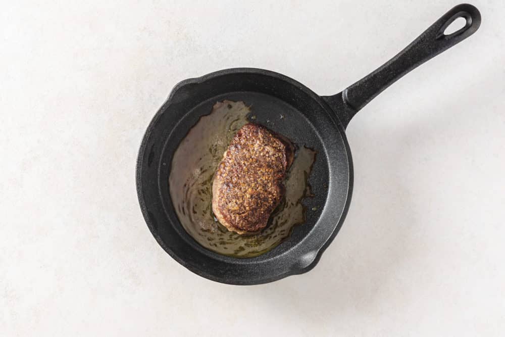 cooking steak in a black pan.