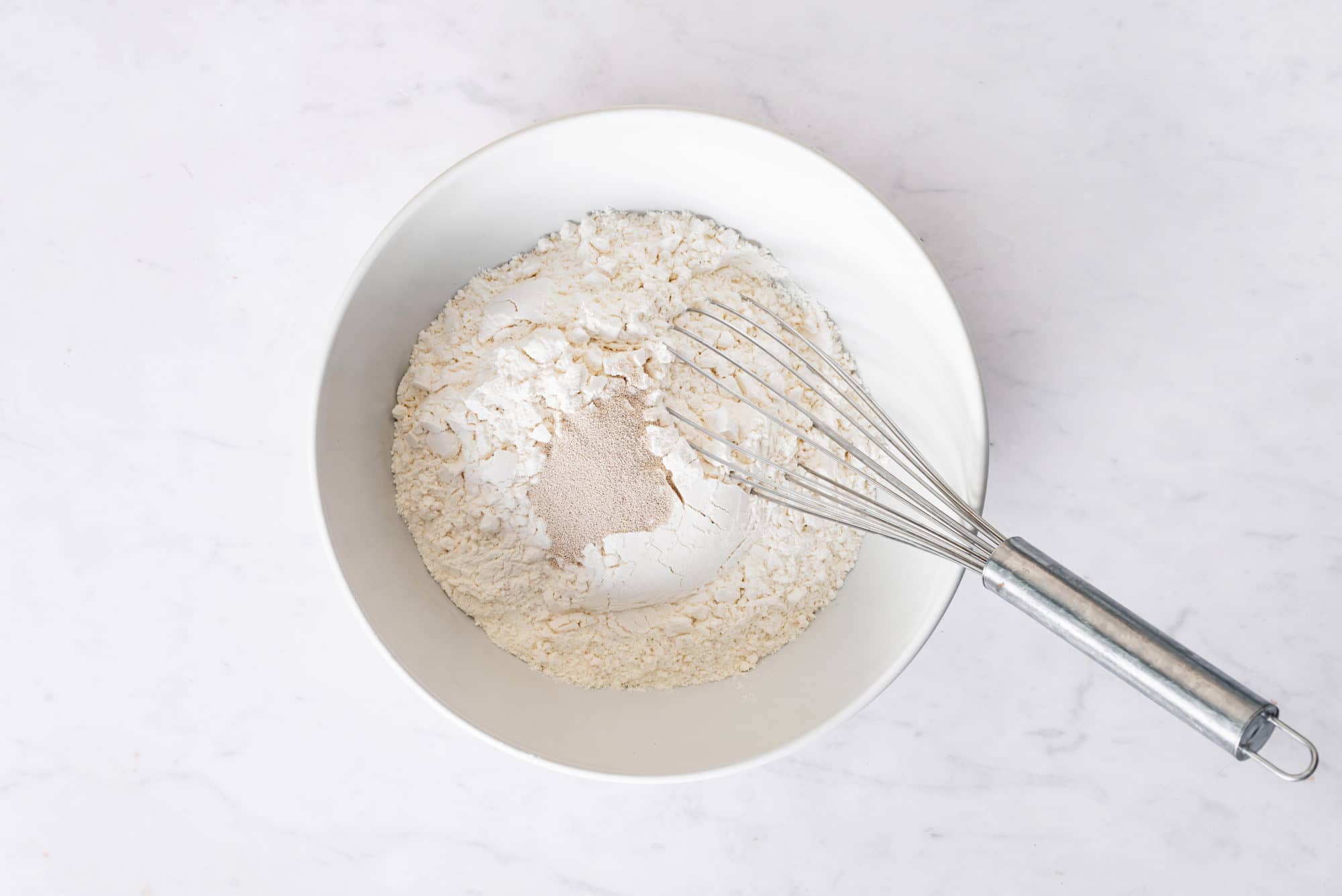 A bowl of dry ingredients for piroshki and a whisk.