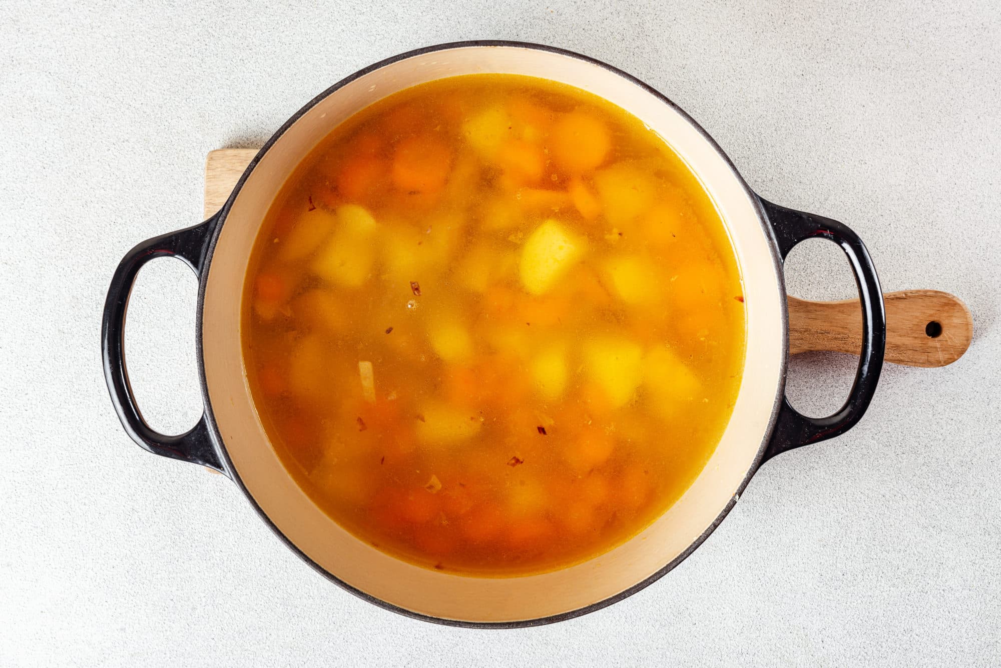 veggies and broth in a black soup pot.