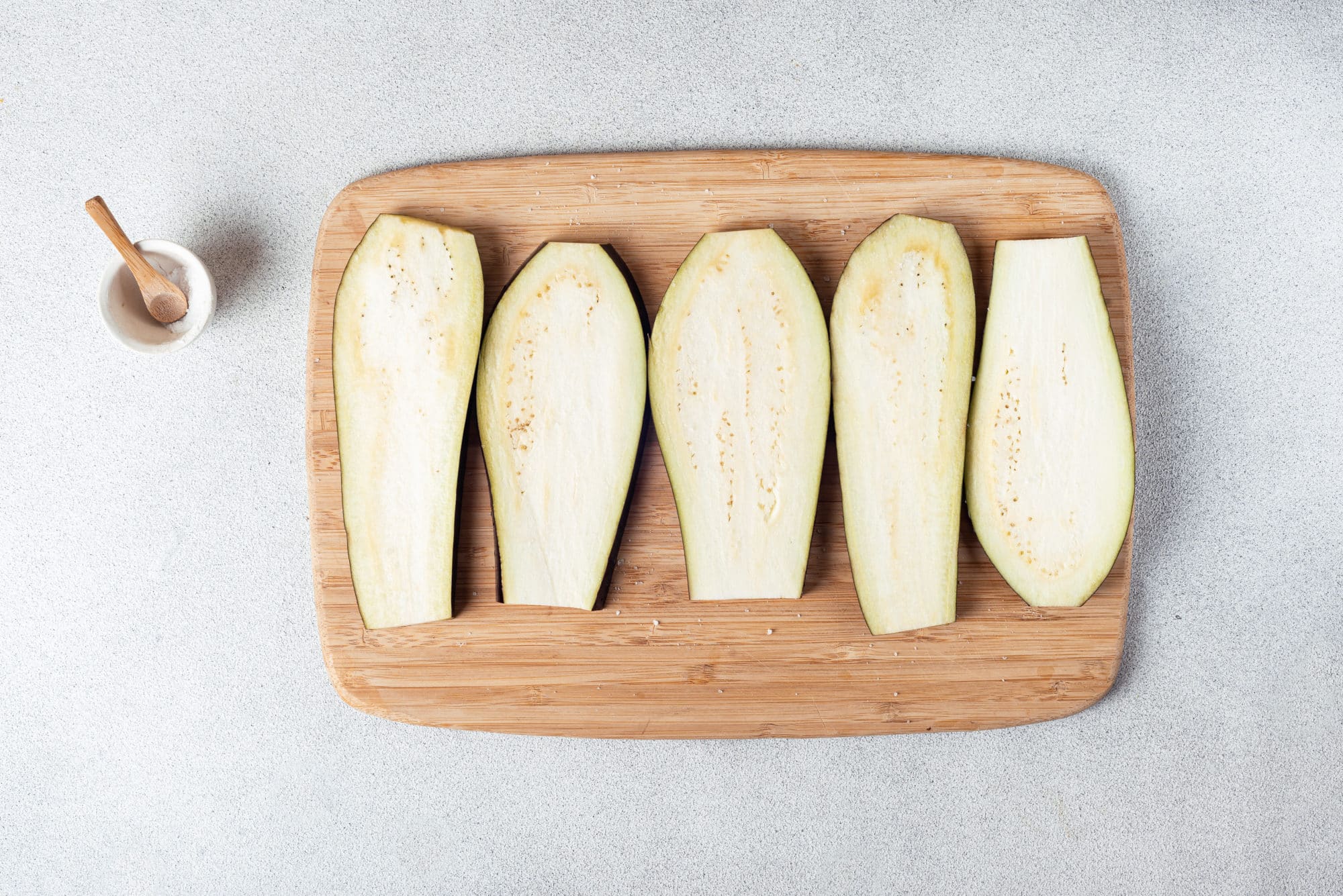 Eggplant slices on a wooden board with salt on the side.