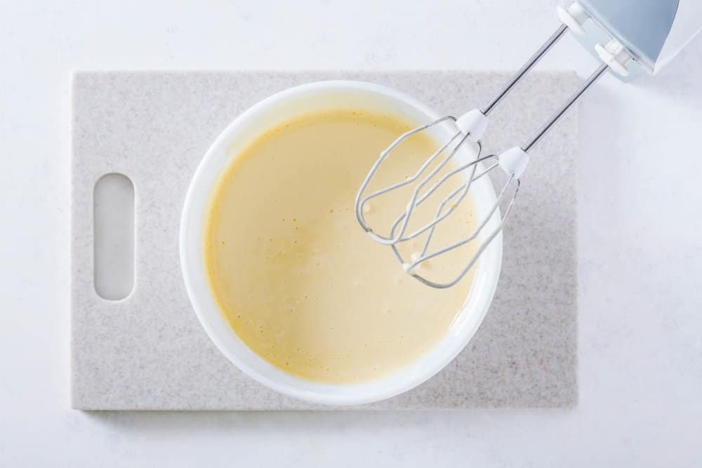 Cake batter in a white bowl on a cutting board with hand mixers.