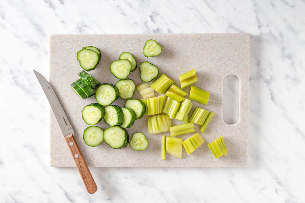 chopped celery and cucumber with a knife on a cutting board.