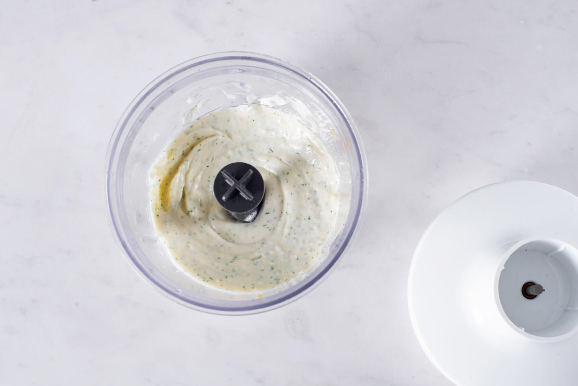 Caesar dressing blended in a food processor with a lid on the side.