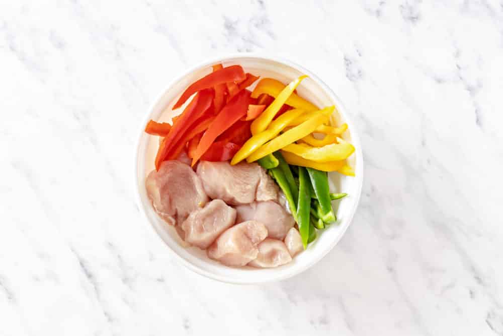 raw chopped veggies and chicken breast in a white bowl.