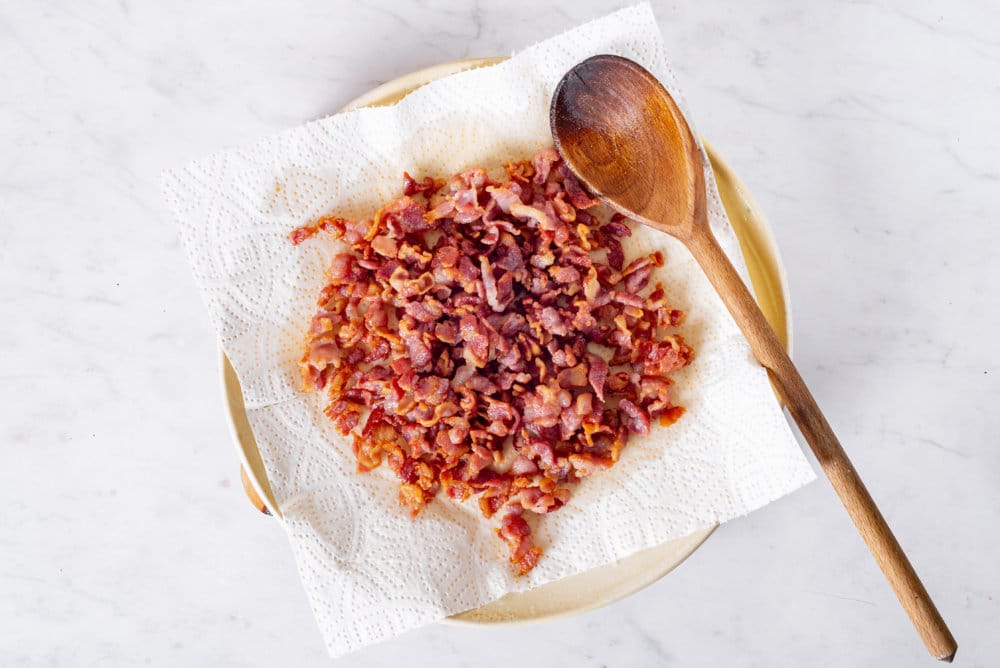 Sauteed bacon on a plate on a paper towel with a wooden spoon on top.