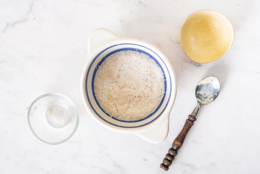 piroshki-dough-process-in-a-blue-bowl-with-a-spoon-and-two-empty-ingredient-bowls-on-the-sides